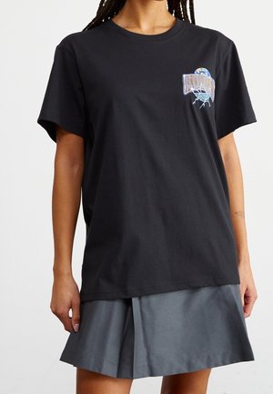 Sort bomulds-T-shirt med korte ærmer, med en farverig grafik på brystet. Kombineret med en grå nederdel med plisseringer.