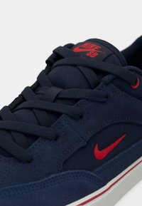 Baskets Nike SB bleu foncé avec logo swoosh rouge, accents rouges, lacets noirs et semelle blanche avec bande rouge.