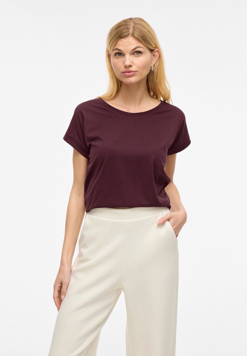 Kratke rokave, krožnega izreza, burgundska majica iz mehke bombažne tkanine, kombinirana z visokim pasom, svetlo kremnimi širokimi hlačami, ki imajo stranske žepke.