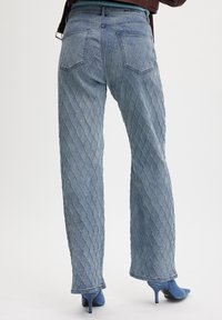 Jeans de mezclilla azul claro con un patrón de diamante texturizado. Diseño de pierna recta con bolsillos traseros y un ligero acampanado en el dobladillo.