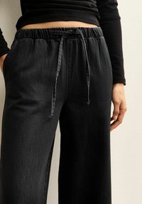 Czarne szerokie spodnie wykonane z miękkiego denimu. Posiadają elastyczny pas z sznurkiem i dwie boczne kieszenie.