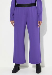 Lila weite Hose aus weichem Material mit einem schwarzen elastischen Bund, der "MODERN VIEW" in erhabenem Text trägt. Glatte Textur, lässiges Design.