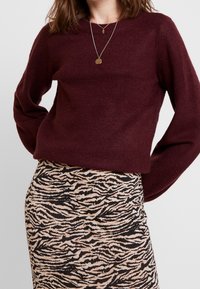 Pull en maille marron à manches longues associé à une jupe beige longueur genou avec un motif de rayures noires façon tigre.