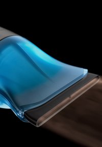 Raclette bleue et noire étalant ou enlevant un liquide sur une surface en bois foncé, avec une vue rapprochée du bord de la lame en caoutchouc.