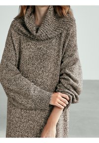 Pull en tricot surdimensionné dans des tons de marron avec un col cheminée, des manches amples et un motif texturé. Matériau doux avec une apparence confortable.
