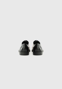 Chaussures en cuir noir avec une finition lisse, bout arrondi et talon bas. Présentent des coutures minimales et un design épuré avec des côtés découpés.