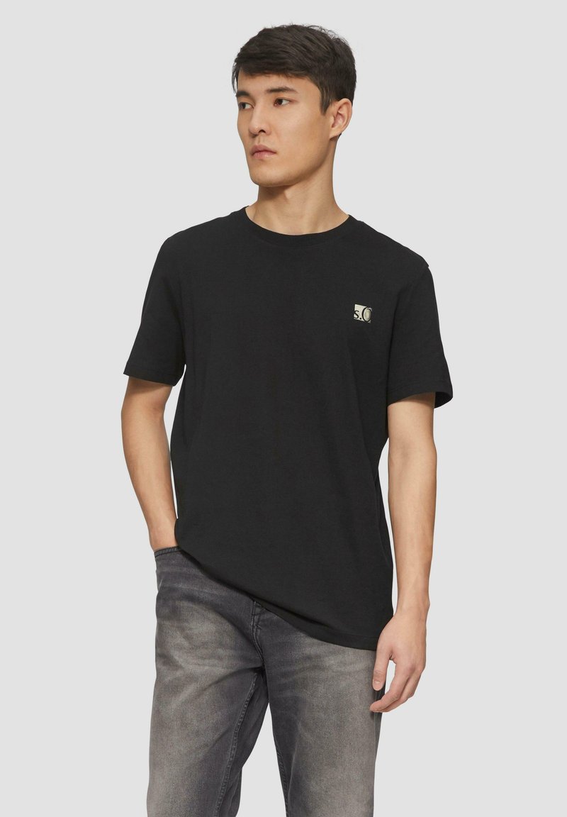 Zwarte katoenen T-shirt met een ronde hals en korte mouwen, voorzien van een klein merklogo op de borst. Gekenmerkt door grijze jeans.