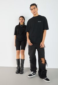 Black oversized t-shirts with a logo, paired with distressed black jeans and knee-high slate boots, against a plain background.