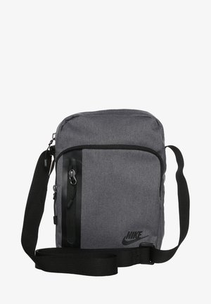 Bolso bandolera gris de Nike con correa negra ajustable, bolsillo frontal con cremallera y logo negro de Nike en el lado inferior derecho.