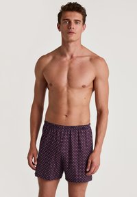 Boxers pour hommes en tissu bleu marine avec un petit motif géométrique en blanc et rouge. Taille élastique, coupe ample, matériau léger et respirant.