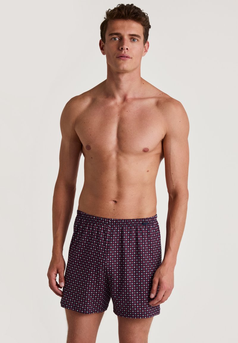 Boxers pour hommes en tissu bleu marine avec un petit motif géométrique en blanc et rouge. Taille élastique, coupe ample, matériau léger et respirant.