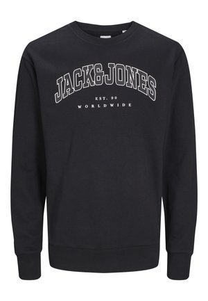 Blond chłopiec stoi z rękami wzdłuż ciała, ubrany w czarną bluzę Jack & Jones, czarne spodnie typu cargo i brązowe trampki na jednolitym tle.