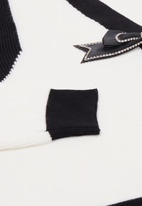 Maglione a maglia con un design bianco e nero, texture a coste e un nastro nero decorato con una forma a stella accentuata in argento.