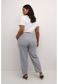Pantaloni grigi chiari con una vestibilità comoda, caratterizzati da una vita elasticizzata e tasche posteriori, abbinati a una camicia bianca a maniche corte e tacchi neri.