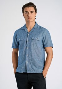 Korte mouwen blauwe chambray blouse met knoopsluiting, twee borstzakken en een camp kraag. De stof heeft een gestructureerde uitstraling.