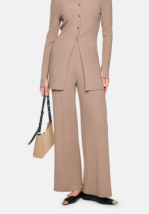 Beige gerippte Strickhose und passende lange Strickjacke mit Knöpfen, schwarze Ballerinas mit goldenen Spitzen und beiger Handtasche mit schwarzem Riemen.