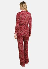 Roter Pyjama mit Blumenmuster, langärmlig und mit Hose, ausgestattet mit rosa Bündchenakzenten und einem Stoffbindegürtel in der Taille.