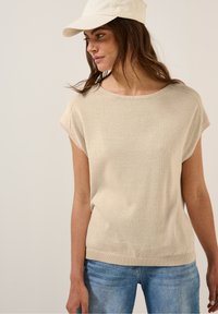 Ljusbeige stickad topp med korta ärmar, rund halsringning och textilstruktur. Kombinerad med ljusblå denimjeans. Enkel, avslappnad design.