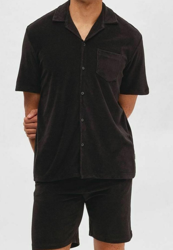 Set di pigiama nero a maniche corte realizzato in tessuto morbido; presenta una camicia con colletto e taschino sul petto, accompagnata da pantaloni corti abbinati.