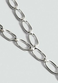 Zilveren metalen ketting met verlengde ovale schakels en een gepolijste afwerking. Vlotte textuur en een uniforme vorm in het geheel.