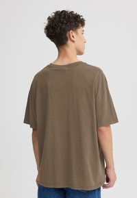 T-shirt en coton marron oversize avec un col rond et des manches courtes, présentant une texture subtile et des détails de couture visibles.