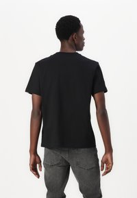 Svart T-skjorte med korte ermer laget av bomull, med rund halslinning og standard passform, kombinert med grå denimjeans.