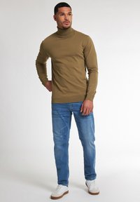 Olivově zelený rolák v kombinaci se světle modrými džínami a bílými teniskami. Svetr má přiléhavý střih a žebrované manžety.