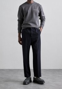 Gray sweatshirt with a crew neck and white text on the chest, paired with navy trousers. Footwear features dark gray sneakers.