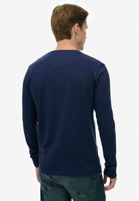 Navy langemouwen shirt van zachte katoen, met een ronde hals en geribbelde manchetten. De achterkant is eenvoudig zonder extra patronen.
