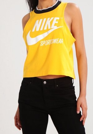 Yellow Nike Sportswear cropped tank top with a black collar and white logo. Paired with black pants, showcasing a fitted design.