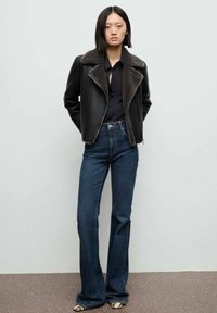 Giacca da biker in pelle nera con colletto in pelliccia grigia, abbinata a jeans a zampa d'elefante blu scuro e tacchi con motivo. Design semplice con una silhouette aderente.