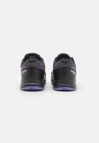 Czarne i fioletowe buty sportowe z teksturowanym wierzchem, wzmocnioną piętą i fioletową podeszwą. Posiadają detale z logo po bokach.