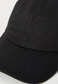 Boné de basebol preto com o logótipo EA7 bordado e o texto "Emporio Armani." Apresenta um tecido texturizado e um design estruturado.