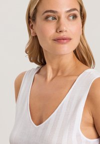 Top sin mangas blanco con un profundo escote en V, patrón de rayas verticales y tejido suave y texturizado. Sin hardware ni acentos visibles.