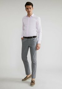 Jasnoróżowa koszula z długim rękawem i zapięciem na guziki, w połączeniu z szarymi spodniami w kratę i brązowymi butami typu boat shoes, o dopasowanym kroju.