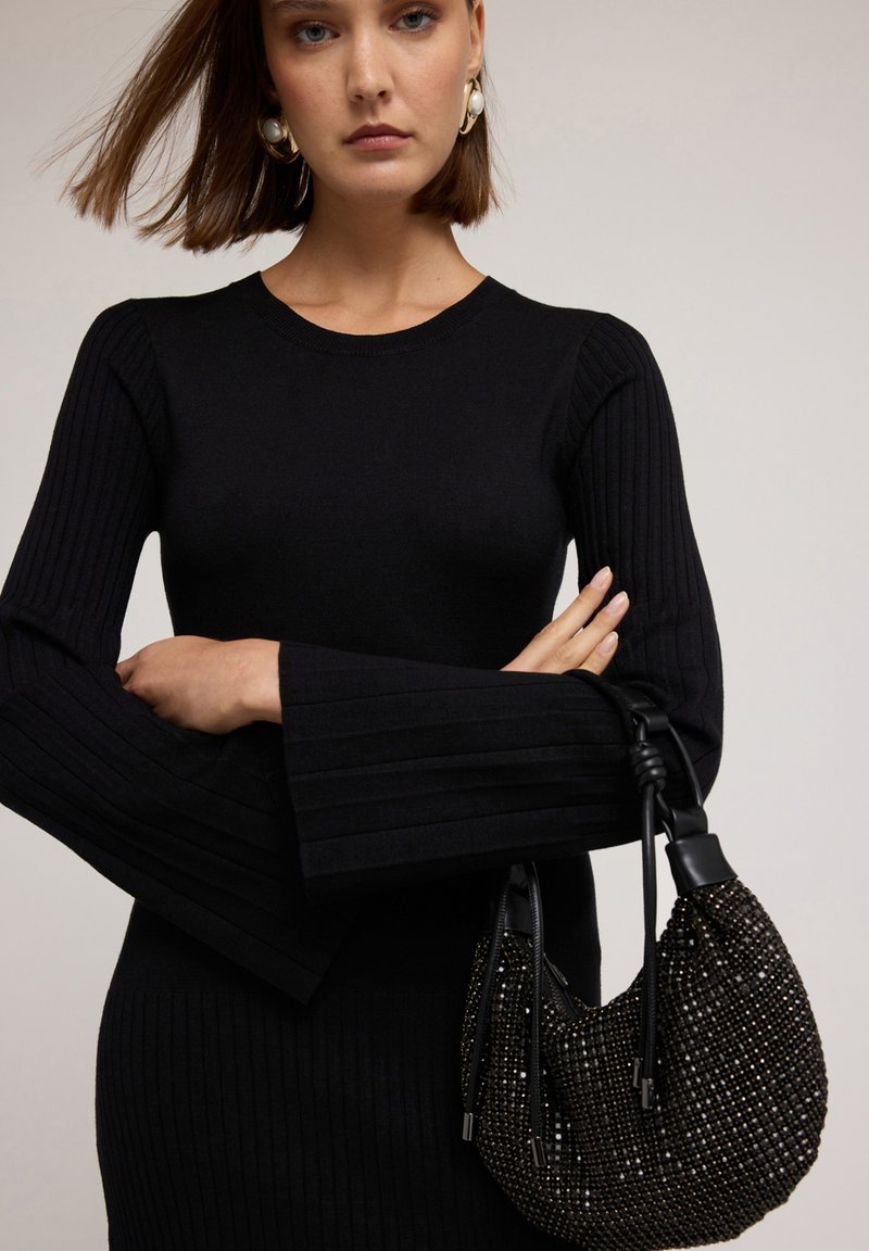 Suéter negro de canalé con mangas acampanadas, combinado con un pequeño bolso negro decorado con cuentas brillantes y elegantes detalles de metal.