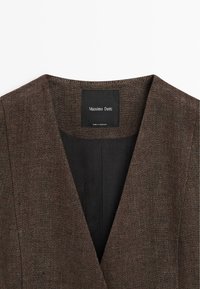 Bruine blazerkraag in visgraatpatroon met zwarte voering en zwart label met de tekst "Massimo Dutti, Made in Morocco."