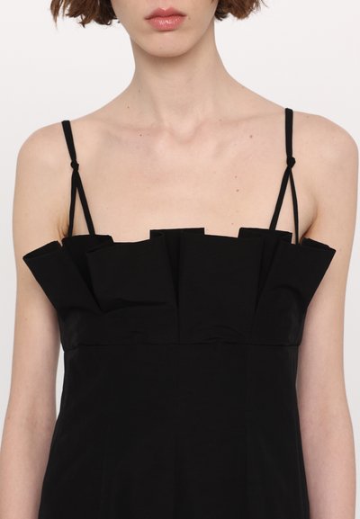 Rochie neagră fără mâneci, cu un corp ajustat și detalii structurate cu volane de-a lungul gulerului. Material neted, design minimalist, bretele ajustabile.