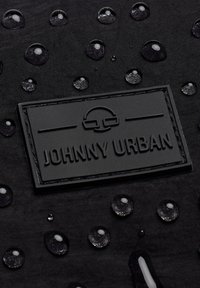 Tessuto nero con gocce d'acqua in rilievo e finitura testurizzata. Un'etichetta nera in rilievo reca la scritta "JOHNNY URBAN" nella parte inferiore.