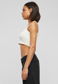 Débardeur blanc court avec des fines bretelles, associé à un pantalon noir taille haute. Tissu lisse avec un design minimaliste, silhouette ajustée.