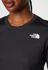 Svart långärmad tröja i ribbad tyg, med en vit logotyp på vänster bröst och rund halsringning.