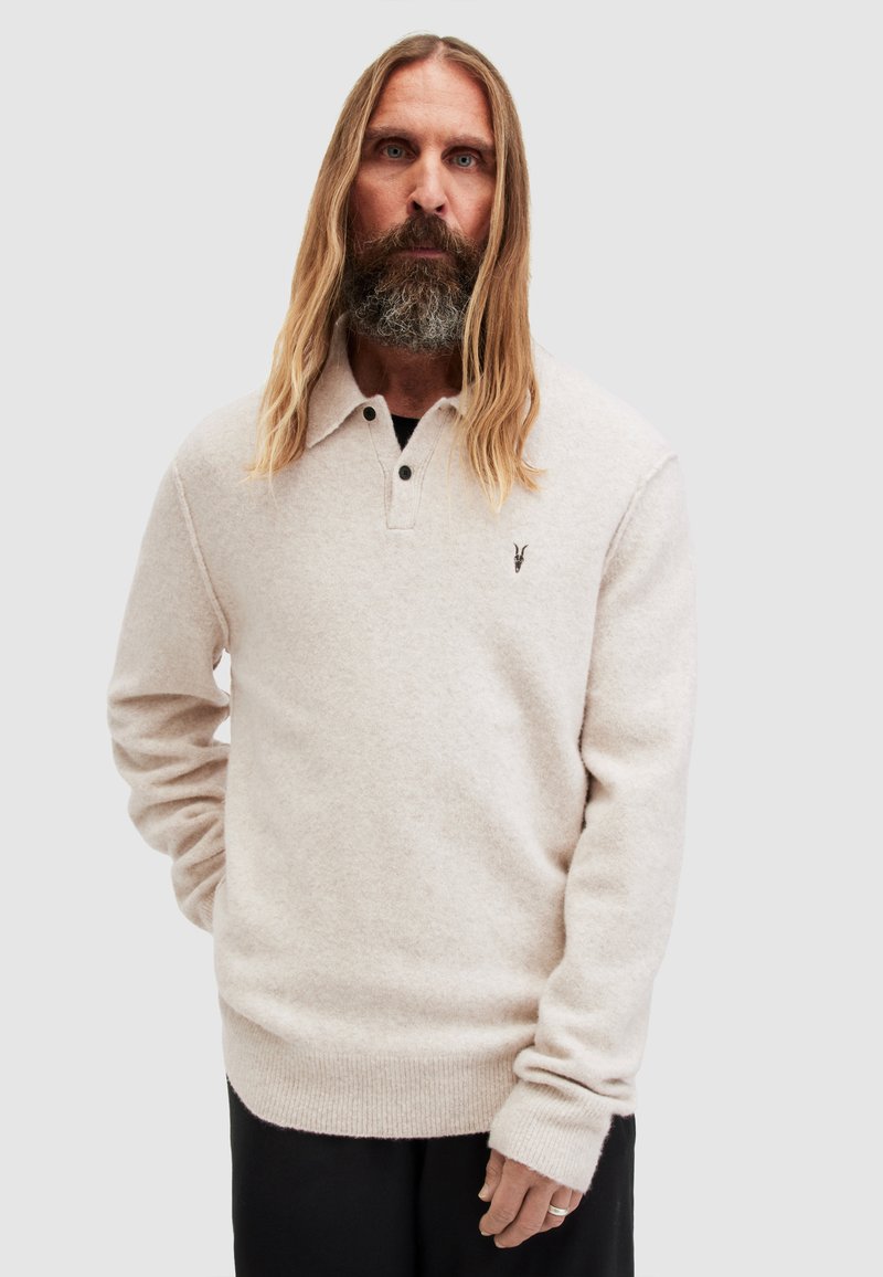 Maglione pullover beige chiaro, texture morbida, maniche lunghe, design con colletto e due bottoni, con un piccolo accento di marca sul petto.
