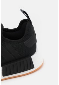 Svart sportskor med övre i strukturerad mesh, gummiskydd på hälen, vit mellansula och sula av gummimaterial. Har svarta randiga detaljer.