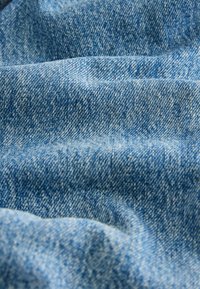 Tessuto denim di colore blu chiaro, con una superficie texture che presenta trame visibili, pieghe e modelli sottili nelle fibre.