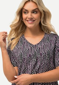 Camiseta de manga corta negra con escote en V, decorada con un patrón de puntos morados y blancos superpuestos, hecha de una tela suave y ligera.