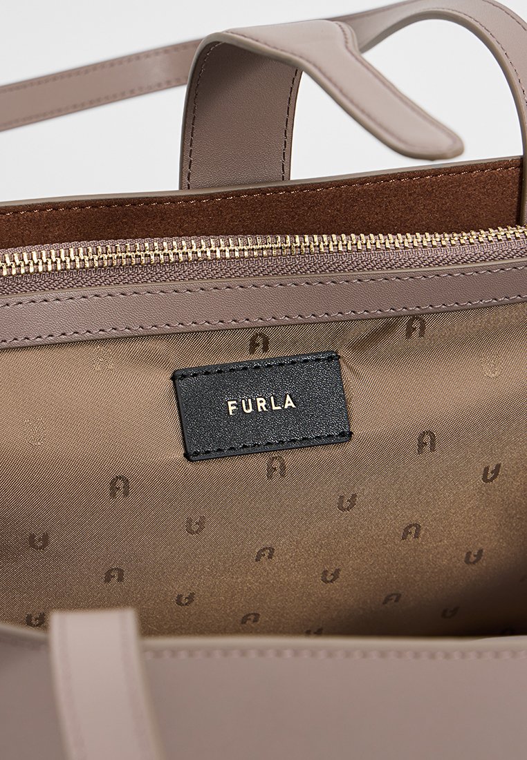 Helle beige Lederhandtasche mit goldfarbenem Reißverschluss, braunem Wildlederfutter und einem schwarzen Stofflabel mit dem in Gold eingeprägten "Furla".