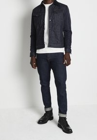 Mörk denimjacka med en texturerad framsida, komplementerad med en vit skjorta och slim-fit mörka jeans. Avslutas med svarta läderstövlar och uppvikta  ärmar.