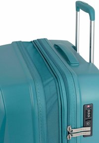 Maleta rígida color teal con doble cremallera, asa de transporte lateral y asa retráctil plateada. Presenta un candado de combinación en la parte frontal.