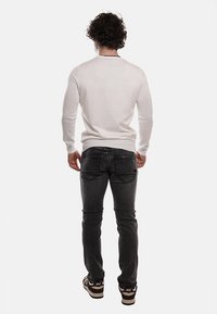 Maglione bianco aderente con maniche lunghe, abbinato a jeans grigio scuro. Dettagli notevoli includono polsini a coste e tessuto a contrasto sulle spalle.