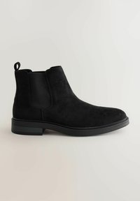 Botín Chelsea de ante negro con paneles laterales elásticos, puntera redonda, tira de arrastre y suela de goma texturizada. Acabado suave con mínimos detalles de costura.